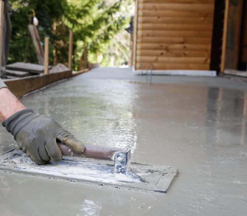 Mason leveling and screeding concrete floor base with square trowel in front of the house. Construction business, do-it-yourself, precision work around the house concept.